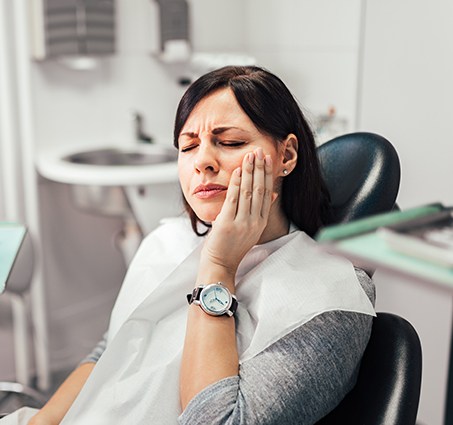 Woman in need of emergency dentistry holding cheek in pain