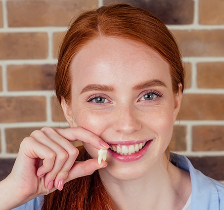 Smiling woman holding up tooth after tooth extraction