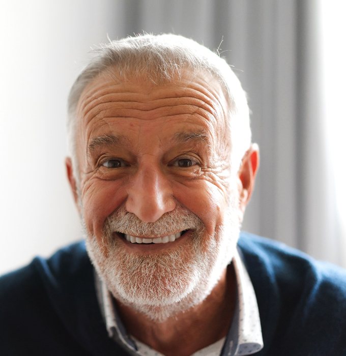 Senior man in front of curtain with implant dentures in Chelsea, MI