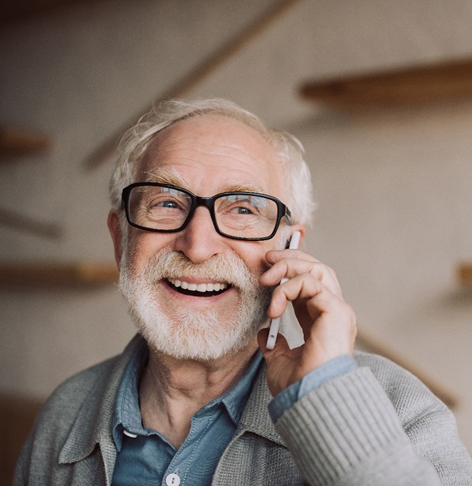 Older man on phone with implant dentures in Chelsea, MI