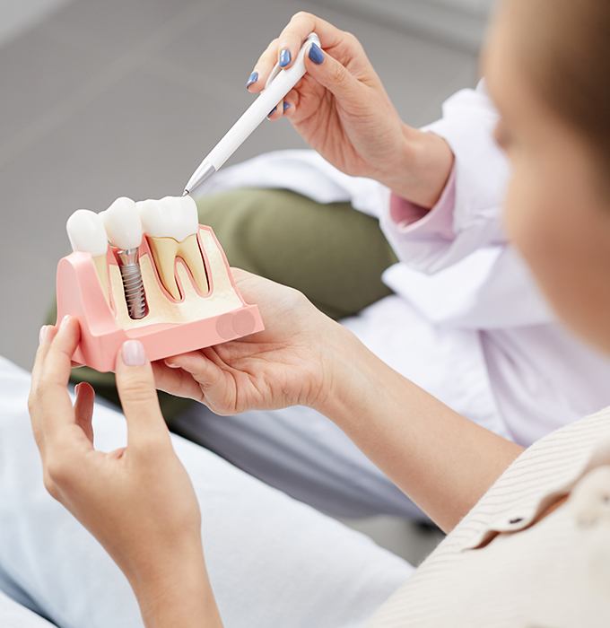 Dentist showing patient model comparing a healthy tooth and dental implant supported replacement