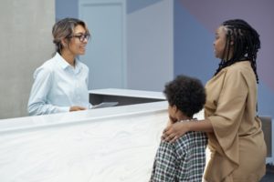 a parent and child speaking with a front desk attendant about dental insurance at a dental office