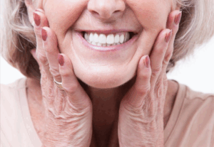 Woman smiling brightly and pressing her hands to her youthful face